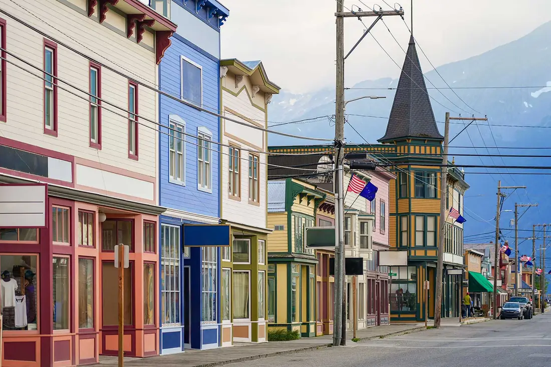 A street of painted wooden shopfronts with mountains behind.