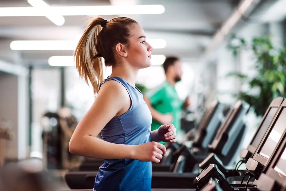A woman running on a treadmill in a row of gym machines.
