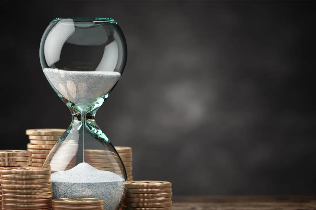 An hourglass running down between stacks of coins.