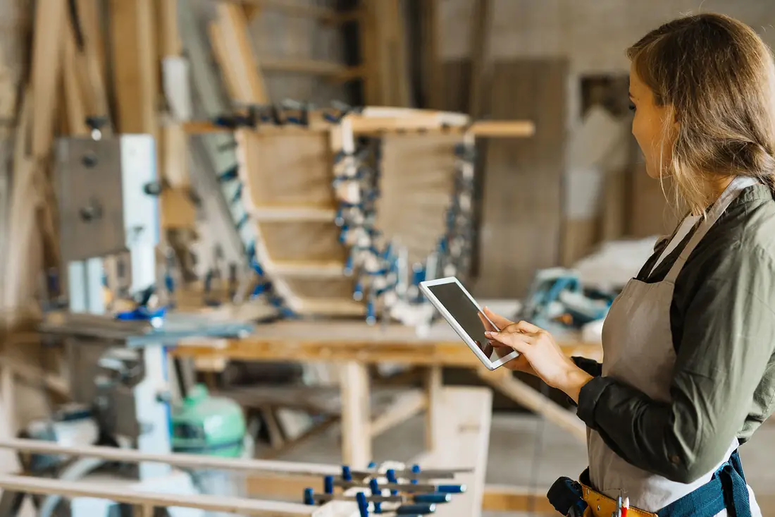 A furniture maker checking a tablet at her bench in the workshop.