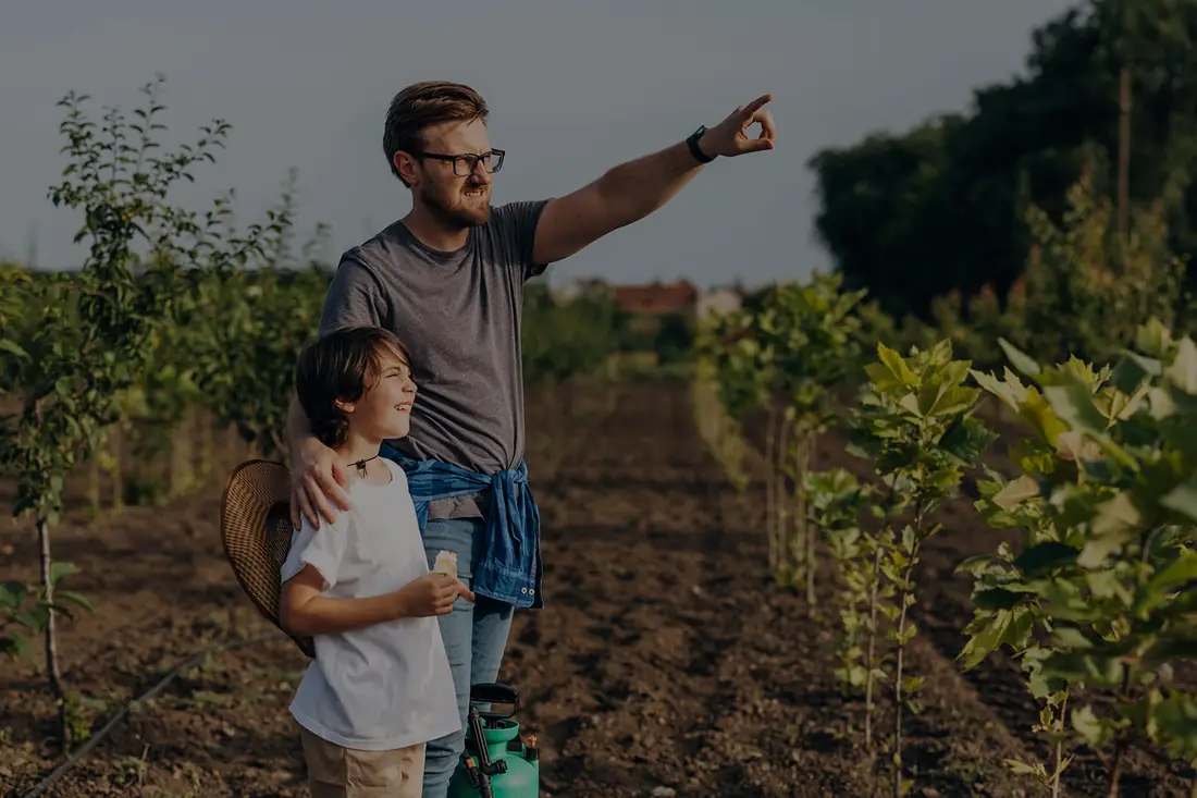 A grower with his son among rows of young trees, pointing out across the field.